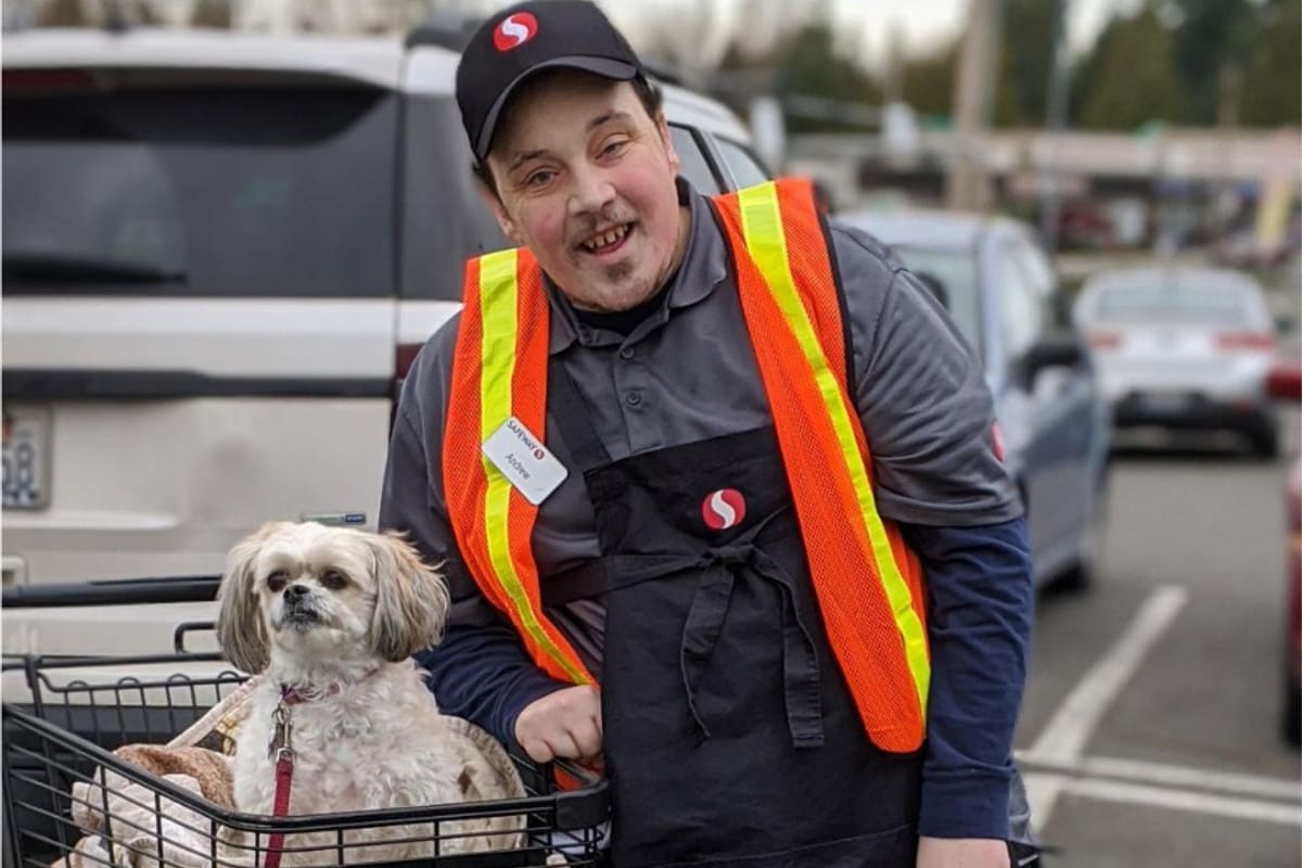 A grocery store employee in a safety vest collecting carts, pausing to greet a customer's dog.