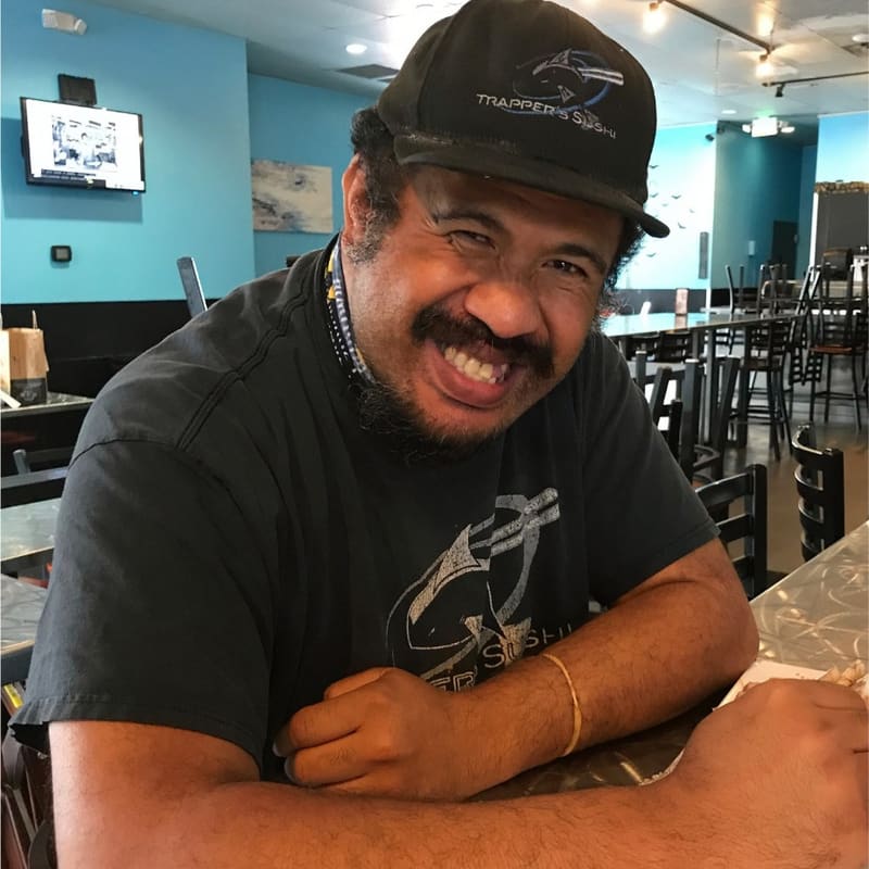 A restaurant team member in a branded cap grinning at his station in the dining room.