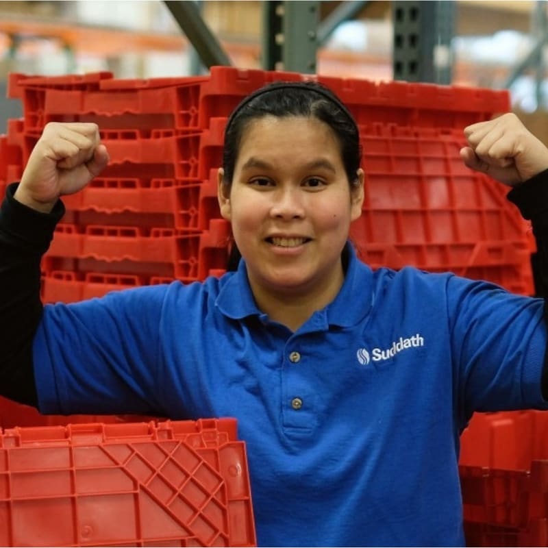A warehouse employee in a company polo flexing both arms in front of a stack of red crates.