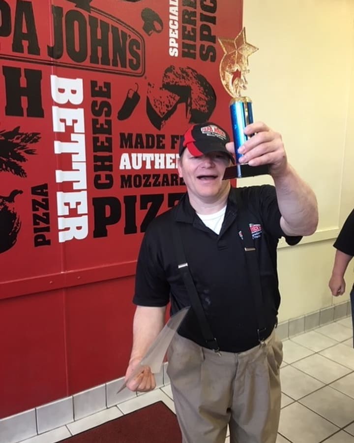 A Papa John's team member in uniform holding up a trophy in the restaurant.