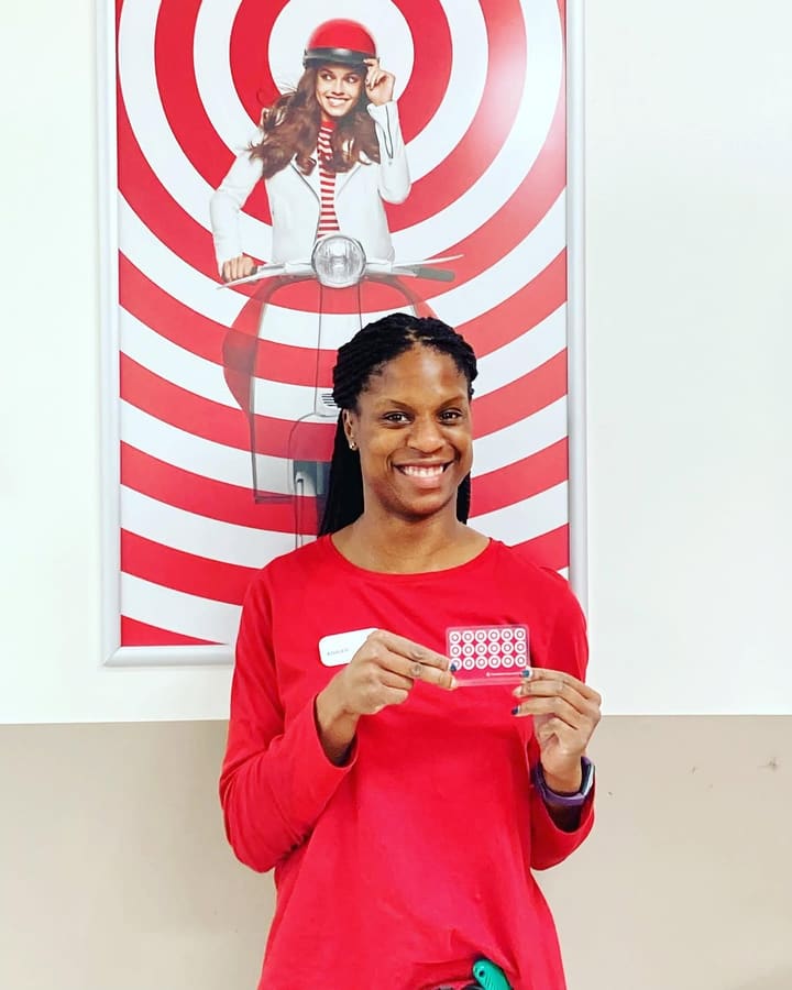A smiling Target team member in her red work shirt, holding a card with the store logo on it.