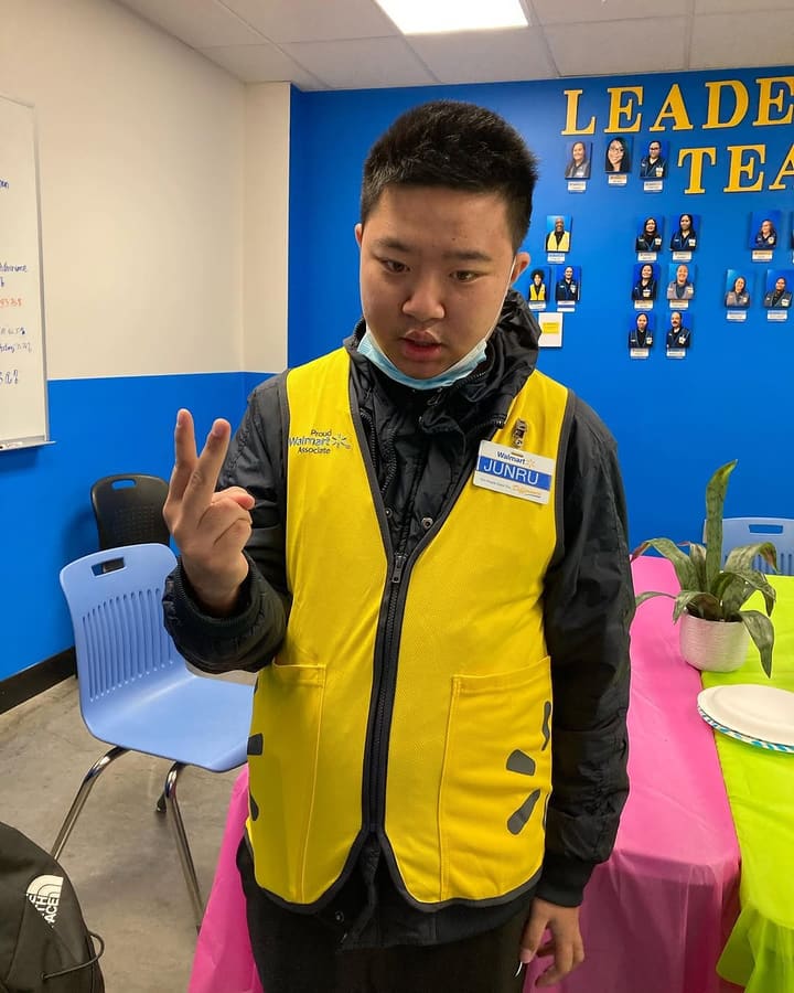 A Walmart associate in his yellow work vest and name badge, celebrating in the store breakroom.