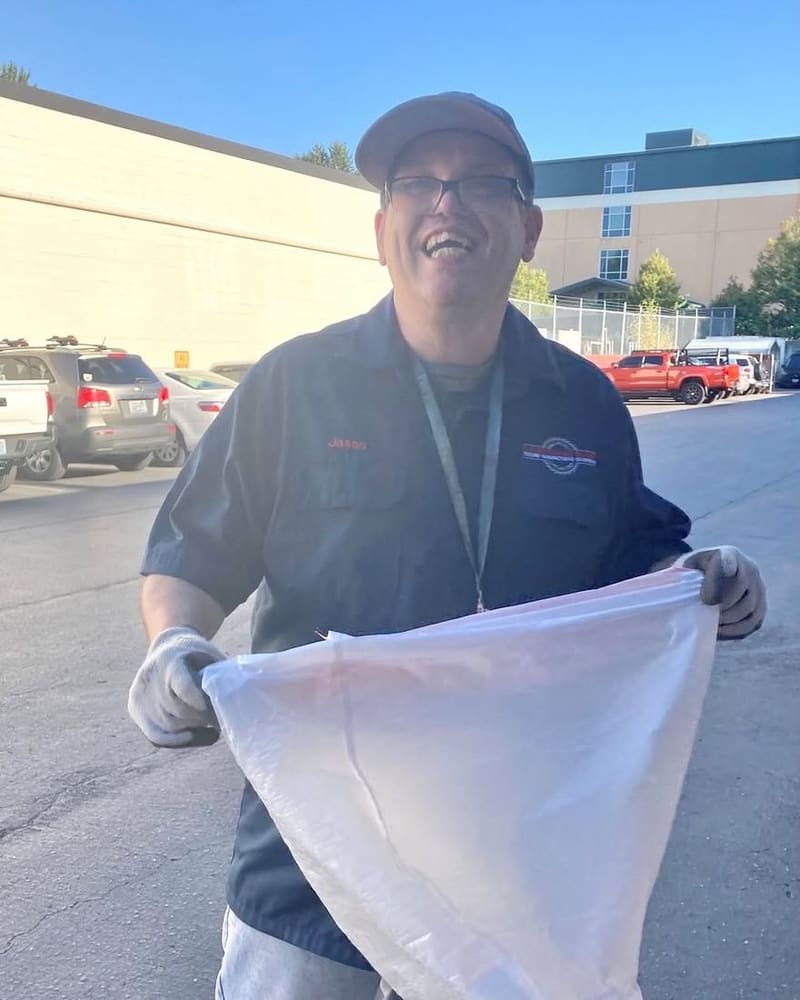 A Vadis-supported employee in his work uniform and gloves, laughing on the job outside on a sunny day.